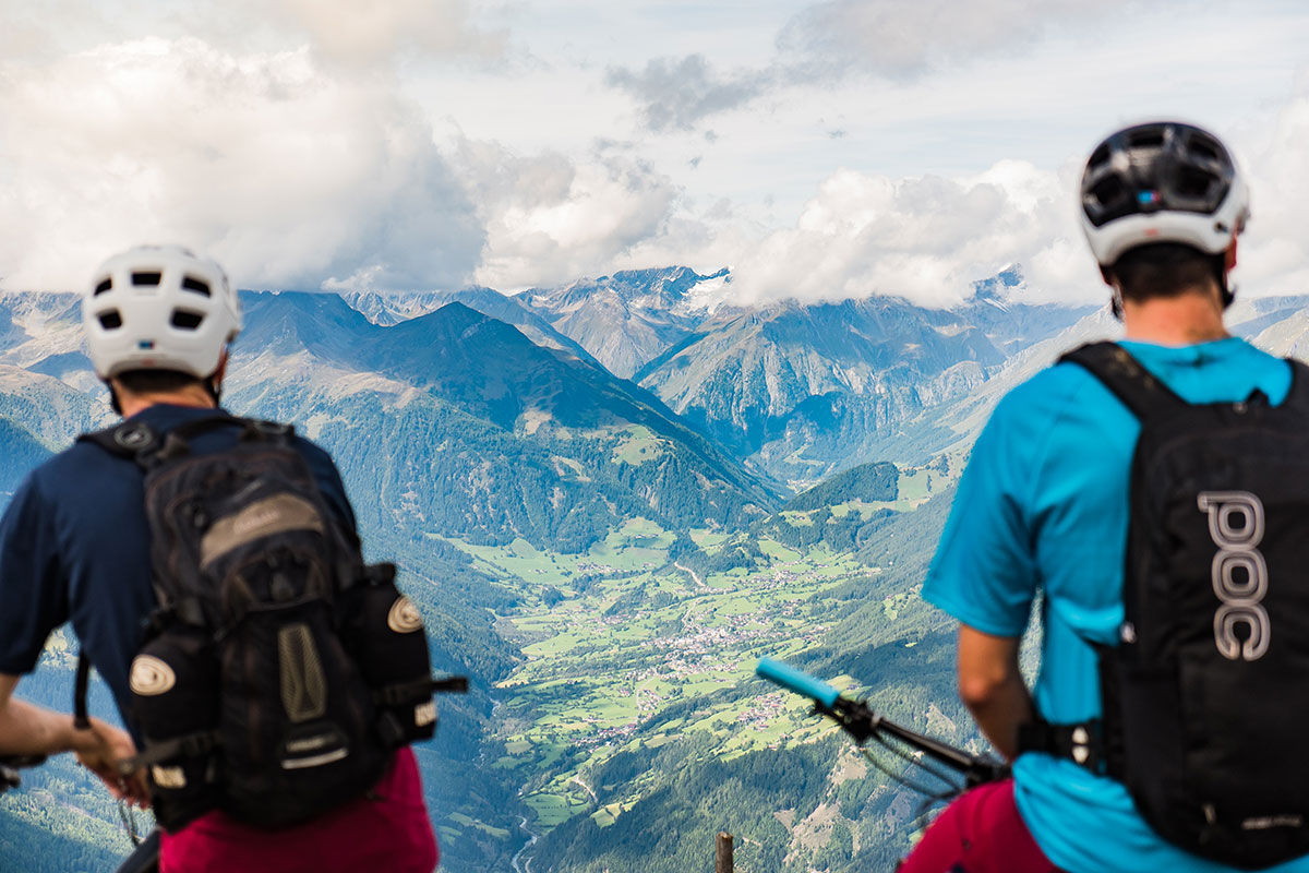 Blick von der Bergstation auf den Adler Trail und das Kalser Tal. Im Hintergrund sind die Gipfel der Hohen Tauern unter Wolken sichtbar.