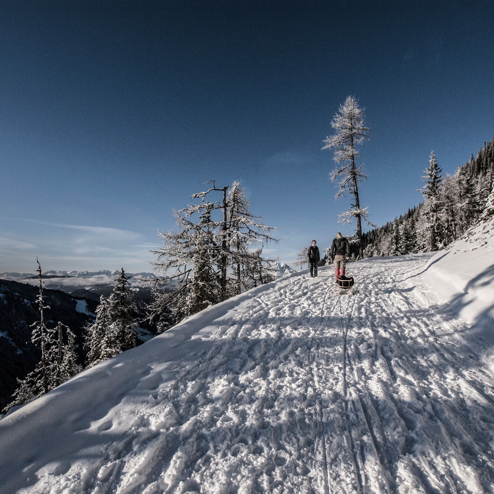 Personen auf dem verschneiten 4-Jahreszeiten-Wanderweg. Die Strecke führt durch eine alpine Winterlandschaft mit Blick auf die umliegenden Berge.