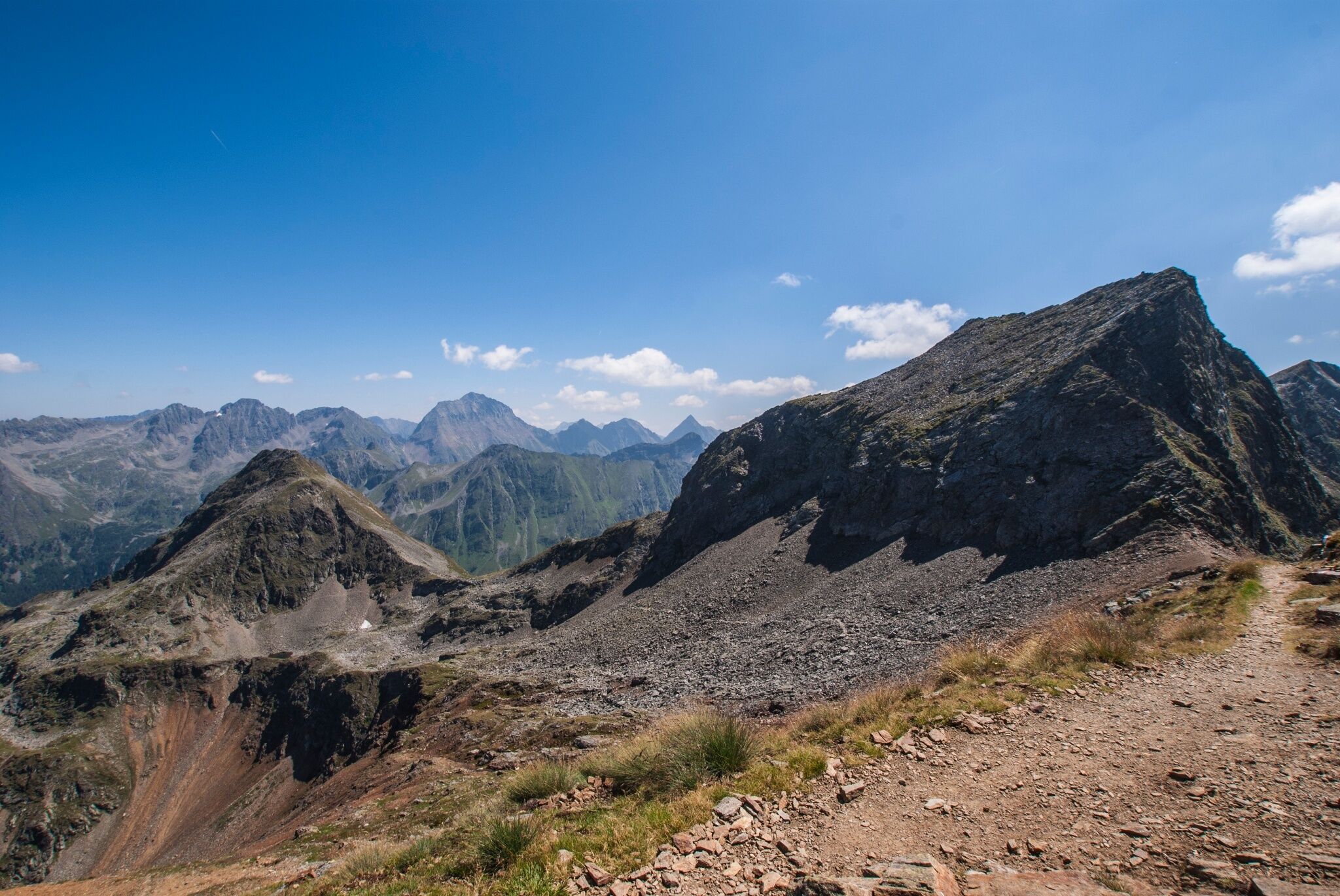 Aussicht von der Rotmandlspitze auf den Sauberg und die umliegende alpine Gebirgslandschaft. Ein schmaler Wanderpfad führt im Vordergrund durch das felsige Gelände.