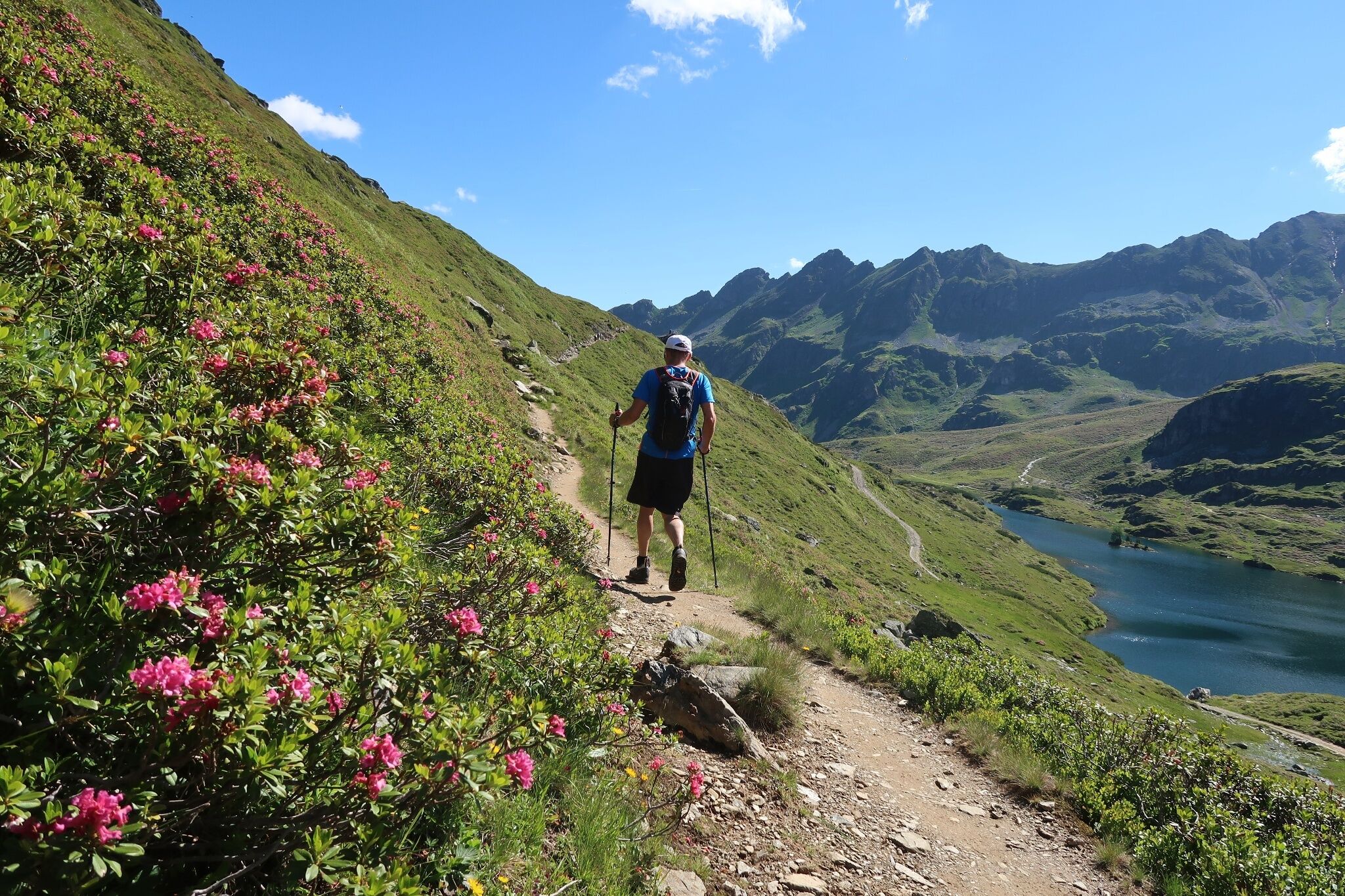 Ein Wanderer begeht einen alpinen Pfad in den Schladminger Tauern. Im Hintergrund sind die Giglachseen und schroffe Berggipfel unter blauem Himmel sichtbar.
