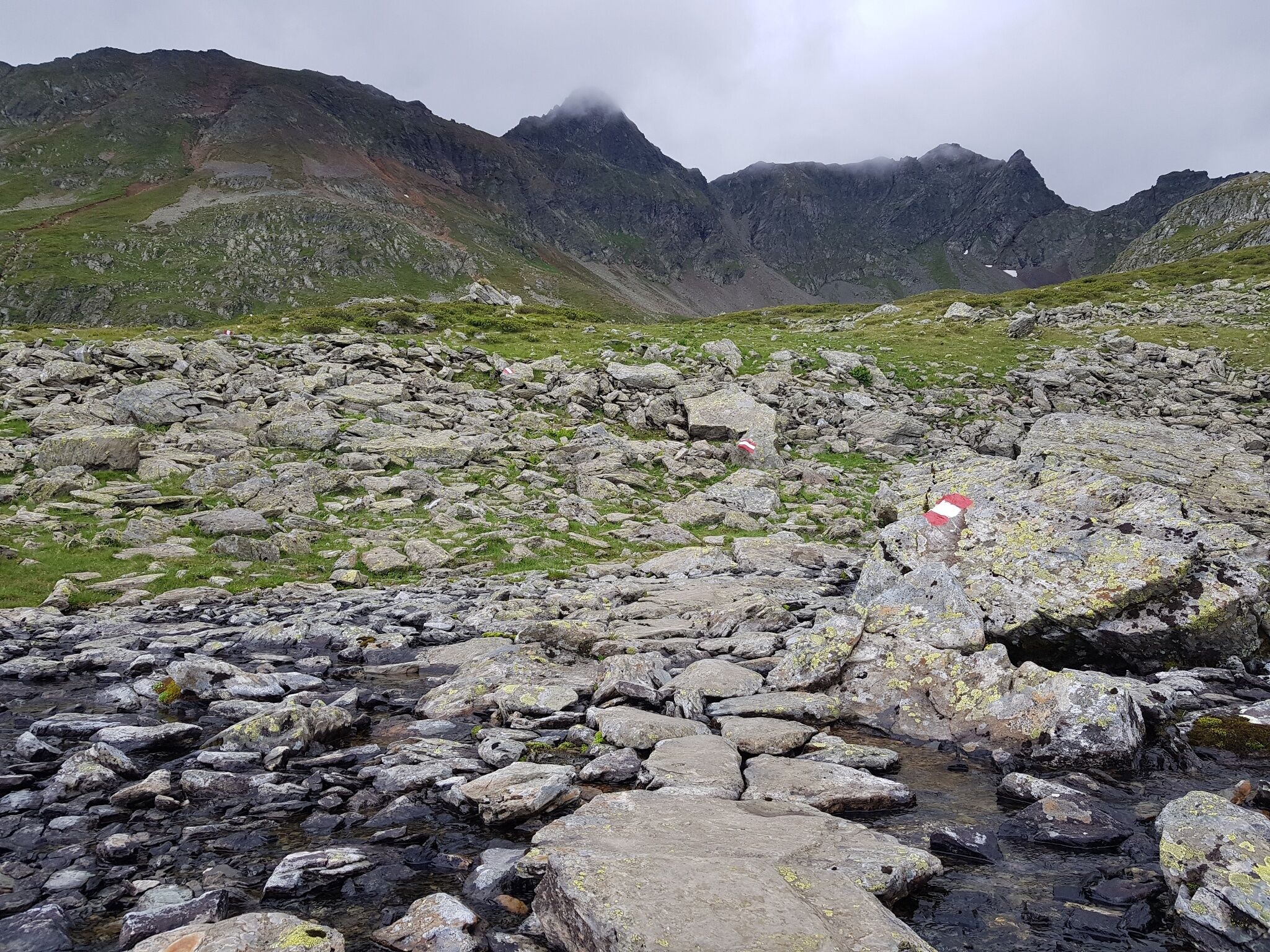 Der markierte Pfad verläuft durch alpines Gelände unterhalb der Rotmandlspitze. Große Steinplatten bilden den Weg durch das Geröllfeld.