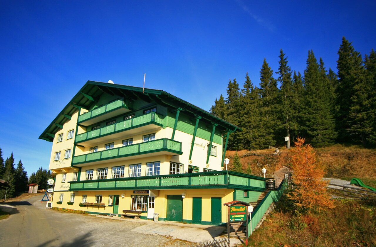 Das mehrstöckige Hotel Planaihof liegt direkt an einem bewaldeten Hang. Das Gebäude verfügt über mehrere Balkonreihen mit grünen Geländern und eine angrenzende Zufahrtsstraße.