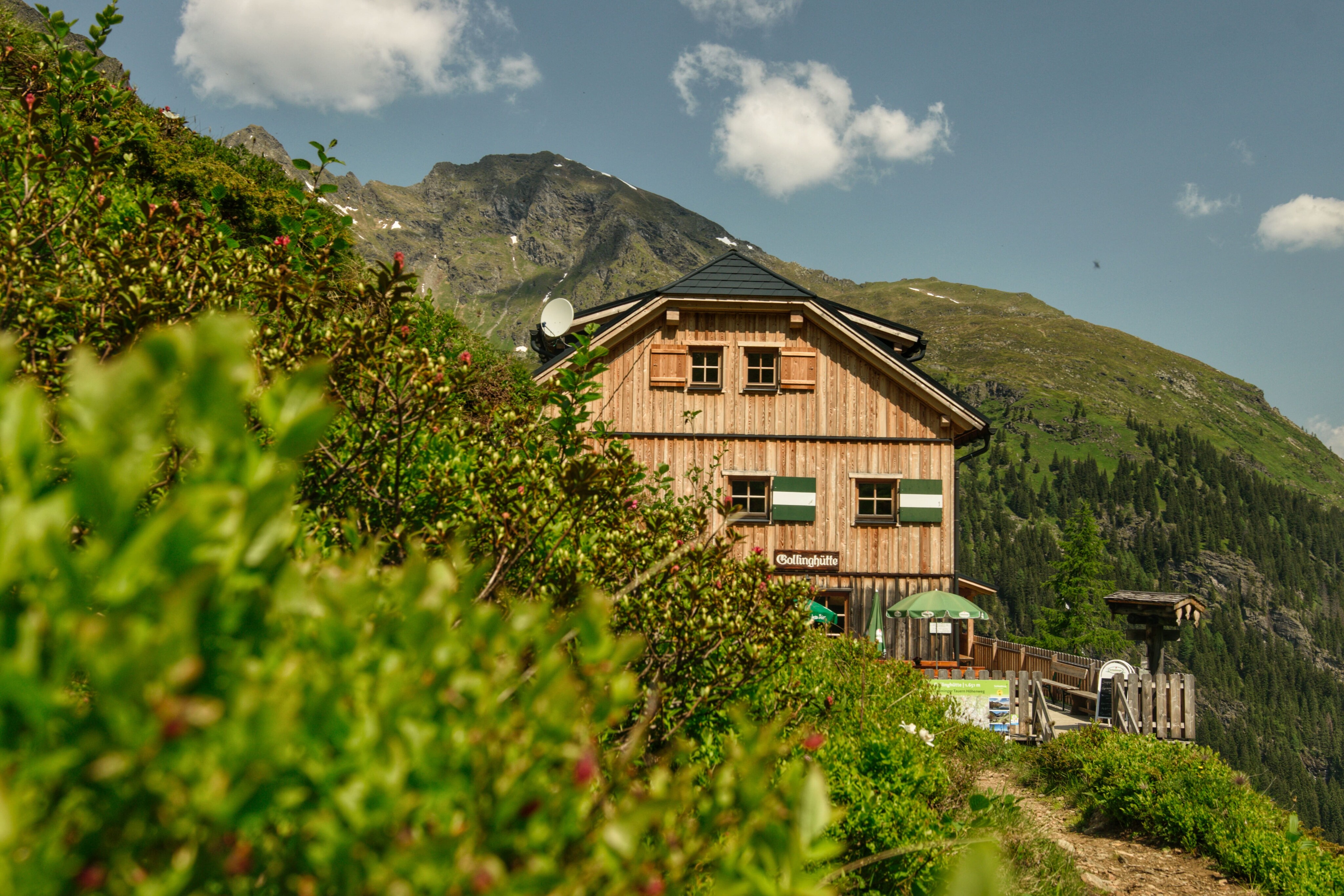 Die Gollinghütte ist ein mehrstöckiges Holzgebäude in den Bergen. Sie liegt an einem Wanderweg und verfügt über eine Terrasse mit Sonnenschirmen.